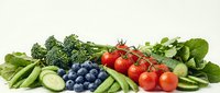 Fresh organic vegetables and fruits arranged on white background including broccoli, cherry tomatoes, blueberries, cucumber, peas and leafy greens for healthy eating.
