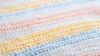 Soft pastel striped crochet baby blanket with delicate texture in pink blue yellow and white colors for nursery decor and infant comfort.