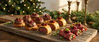 Festive holiday appetizers with cranberry sauce on wooden board near Christmas tree with warm lights and candles creating cozy seasonal atmosphere.