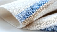 White linen kitchen towel with blue and beige stripes folded on surface. Natural cotton fabric textile for cooking, cleaning and home decor applications.