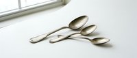 Elegant stainless steel spoons arranged on white surface near window with natural lighting for kitchen dining and culinary photography concepts.