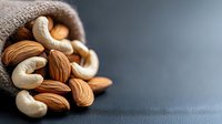 Raw cashews and almonds spilling from burlap sack on dark background, macro food photography with selective focus and copy space for healthy eating concept.