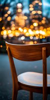 Wooden chair against blurred bokeh lights background creating cozy evening atmosphere. Artistic composition with warm glowing city lights and furniture detail.