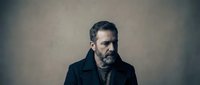 Mature bearded man in dark coat with contemplative expression against textured background for professional portraits and character studies.