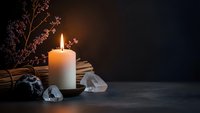 Burning candle with crystals and dried flowers creates peaceful meditation atmosphere on dark wooden surface for wellness and spiritual practices.