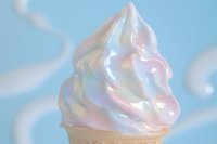 Soft serve ice cream cone with rainbow holographic swirls against dreamy pastel blue sky with fluffy white clouds for summer dessert concepts.