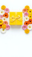 Yellow gift box with ribbon surrounded by colorful spring flowers including gerbera daisies and ranunculus on white background for celebrations and holidays.