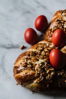 Traditional Easter bread wreath decorated with red dyed eggs and chopped nuts on marble background, close-up view with selective focus and natural lighting.