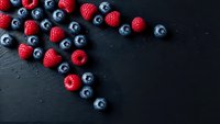 Fresh mixed berries raspberries and blueberries scattered on dark slate background with copy space for healthy food and nutrition concepts.