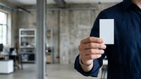 Man in dark business casual shirt holding blank white card in modern office space with industrial interior design.