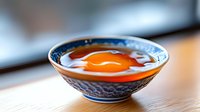 Raw egg yolk in traditional Asian blue and white porcelain bowl on wooden table, macro food photography with selective focus and soft lighting.