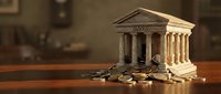 Miniature bank building model with scattered coins on wooden surface representing financial savings and investment concepts for business presentations.