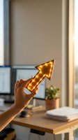 Hand holding illuminated golden arrow pointing upward in modern office workspace symbolizing growth, success and business progress.