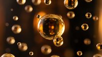 Golden oil bubbles floating in dark liquid creating abstract luxury cosmetic background with warm lighting effects.