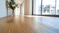 Sunlit wooden floor with natural oak grain texture in modern minimalist room interior, featuring glass vase with greenery and large window view.