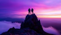 Silhouettes of two hikers standing on mountain peak against dramatic purple and pink sunset sky, with misty clouds below creating ethereal atmosphere.