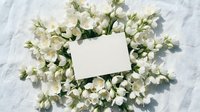 Blank white card surrounded by fresh white flowers and green foliage on marble surface, overhead view for wedding invitations, greeting cards, and event announcements.