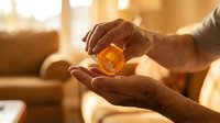 Senior adult hands holding amber glass bottle of essential oil or perfume in warm home interior with golden sunlight.