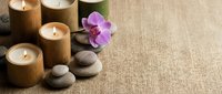 Spa wellness setup with bamboo candles, orchid flower and zen stones on natural burlap background for relaxation and meditation therapy treatments.