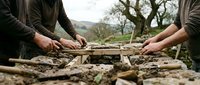 Two people working together building wooden structure outdoors with natural landscape background for teamwork and construction projects.