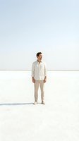 Man in casual beige linen shirt and pants standing alone on empty white salt flat or beach, looking away. Minimalist portrait for lifestyle, fashion, and wellness concepts.
