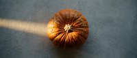Orange pumpkin with deep ridges and natural stem on textured surface with dramatic lighting creating warm shadows for autumn harvest designs.