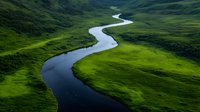 Meandering river flows through lush green valley with vibrant grass meadows and rolling hills, aerial view capturing natural curves and pristine wilderness landscape.