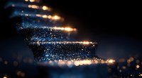 Magical glowing particles swirling in dark space with golden light trails and blue sparkles creating ethereal atmospheric effect against black background.