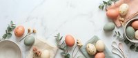 Easter eggs in pastel colors with eucalyptus branches and ceramic bowls on white marble background. Spring holiday decoration and celebration concept.