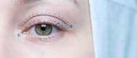 Close-up of young woman's eye with creative makeup featuring colorful dots and stars around eyelid for beauty and cosmetic concepts.