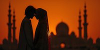 Romantic couple silhouette against orange sunset with mosque minarets in background creating intimate moment for wedding and love concepts.