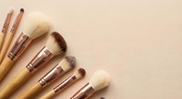 Professional makeup brushes with wooden handles and rose gold ferrules arranged on neutral beige background for beauty and cosmetics applications.