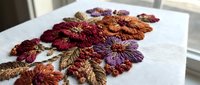 Colorful embroidered flowers with rich burgundy, orange and purple petals on white fabric showcasing detailed needlework and textile artistry for crafting projects.