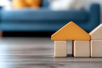 Wooden toy blocks arranged as simple house shape with orange roof on gray surface, symbolizing real estate, property investment and home ownership concept.