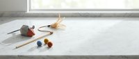 Minimalist marble bathroom counter with natural light, wooden toothbrush, colorful bath accessories and dried flower creating serene spa-like atmosphere.
