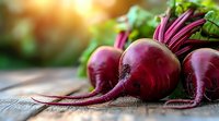 Fresh organic beetroots with green leaves on rustic wooden background in natural sunlight. Close-up view with selective focus and copy space for healthy eating concept.