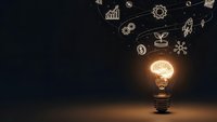 Glowing light bulb with brain filament surrounded by business innovation icons on dark background representing creative ideas and entrepreneurship solutions.