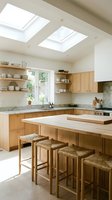 Modern kitchen interior with natural wood cabinets, skylights, and breakfast bar featuring woven stools for contemporary home design and renovation projects.