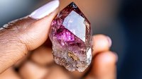 Raw amethyst crystal point with deep purple zones and clear quartz inclusions held between fingers showing natural mineral formation and metaphysical properties.