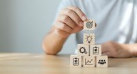 Business professional stacking wooden blocks with strategy icons including target, lightbulb, gears and charts for goal achievement and planning concepts.