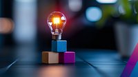 Glowing light bulb balanced on colorful wooden blocks against dark background with bokeh lights, representing creative innovation and bright ideas.