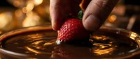 Ripe strawberry being dipped into melted chocolate with warm golden bokeh background, suitable for food photography, culinary blogs, recipe websites, and dessert marketing materials.