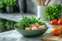 Fresh shrimp with aromatic dill and herbs in green ceramic bowl on marble countertop, selective focus with blurred tomatoes and kitchen herbs background.