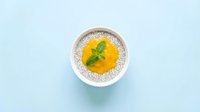 Creamy pumpkin soup with fresh mint garnish served in white bowl on light blue background for healthy autumn cooking and restaurant menu design.