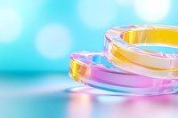 Colorful transparent acrylic or glass rings stacked together against blurred turquoise background with bokeh effect, creating vibrant reflections.