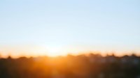 Blurred golden sunrise over distant landscape with warm orange and yellow tones creating serene dawn atmosphere, suitable for backgrounds and wellness content.