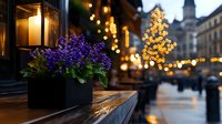 Evening cityscape with glowing lantern and purple flowers in window box against blurred bokeh lights and historic architecture background creates cozy atmosphere.