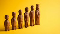 Wooden figurines representing human evolution and growth stages arranged in ascending order on bright yellow background for business and development concepts.