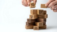 Hands building wooden block tower with business icons for strategic planning and corporate development concepts.