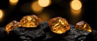 Golden amber gemstones on dark charcoal surface with warm bokeh lights creating luxury jewelry display for precious stone collection and mineral showcase.